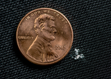 Comparison showing a lethal dose of fentanyl (approximately 2mg of white powder) next to a US penny.